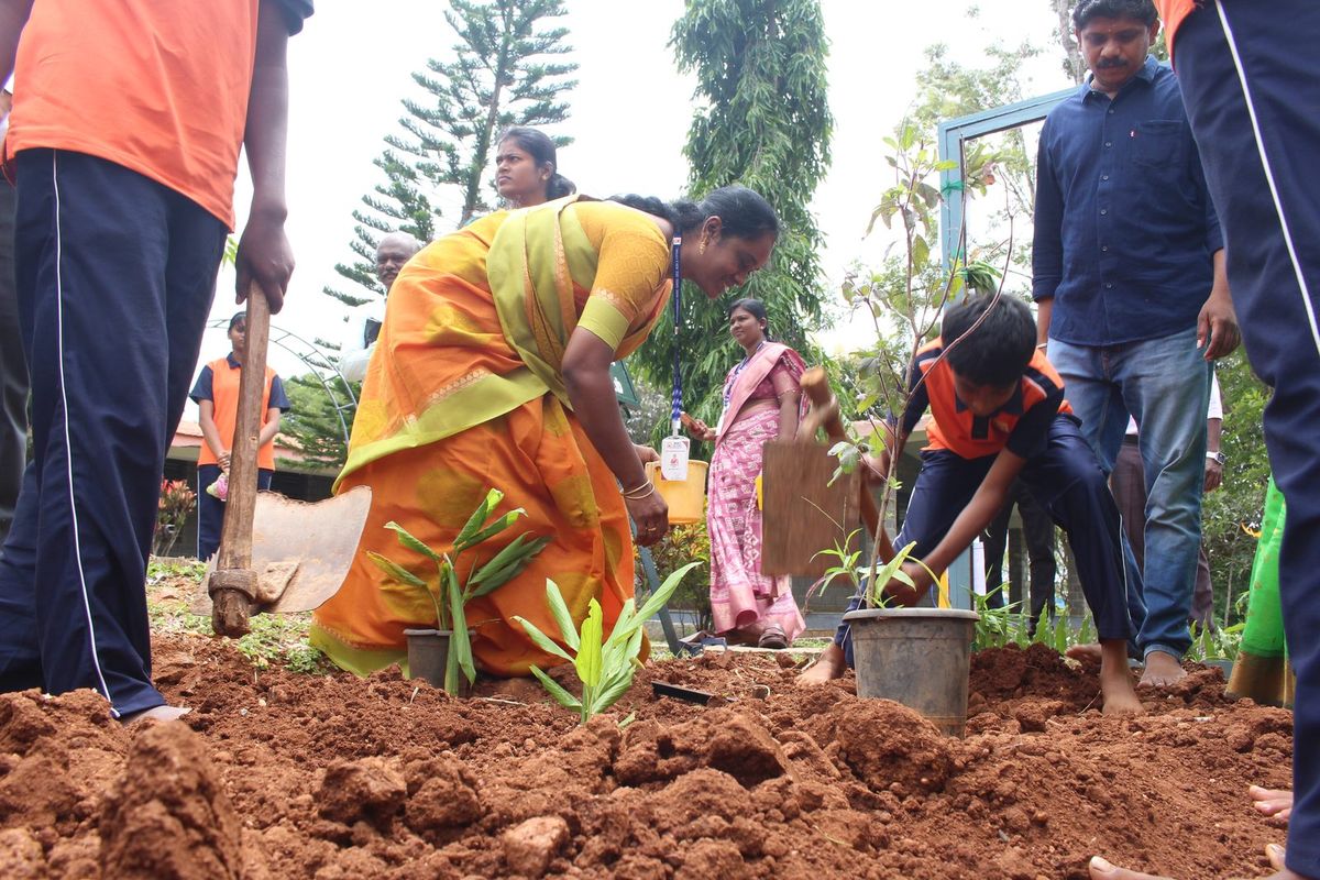 A teacher and students planting saplings in freshly turned red soil