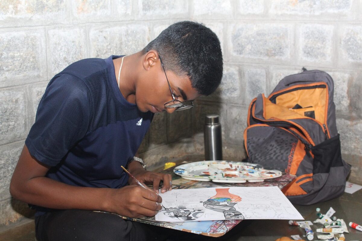 A student sketching an artwork with a paint palette beside him