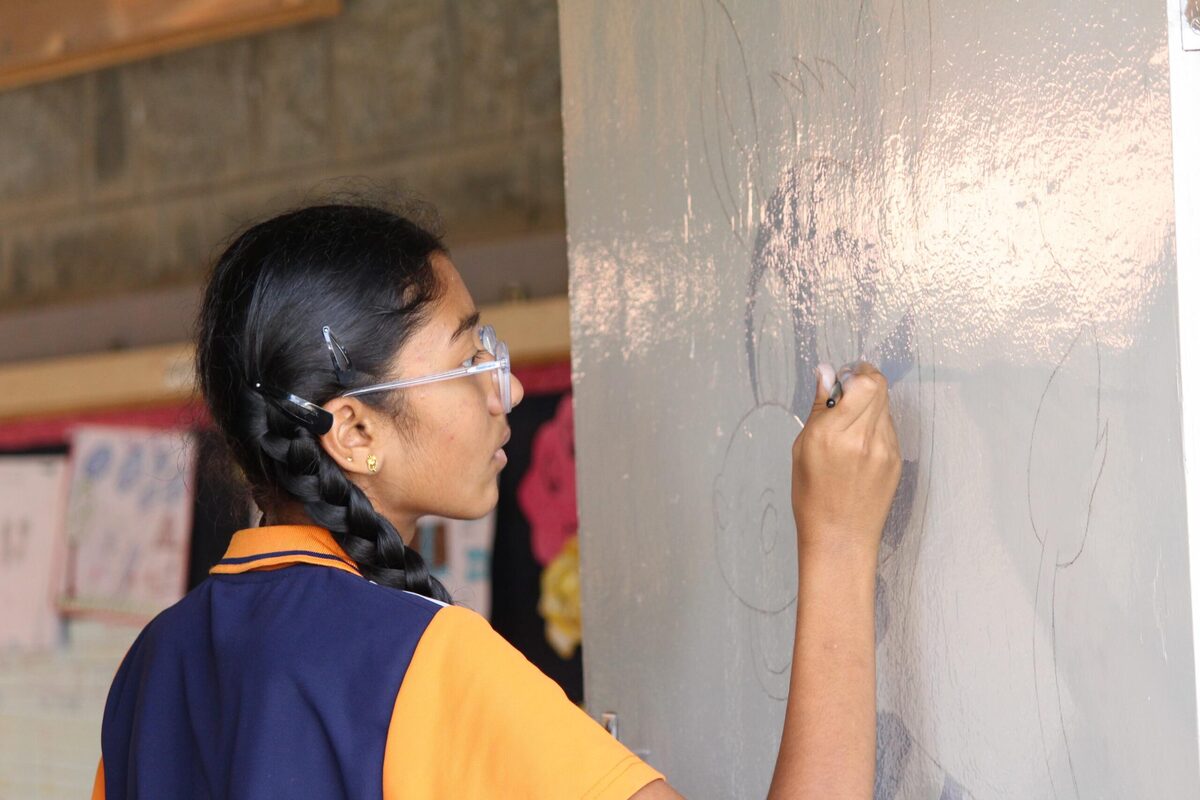 A student sketching a mural outline on a pillar wall