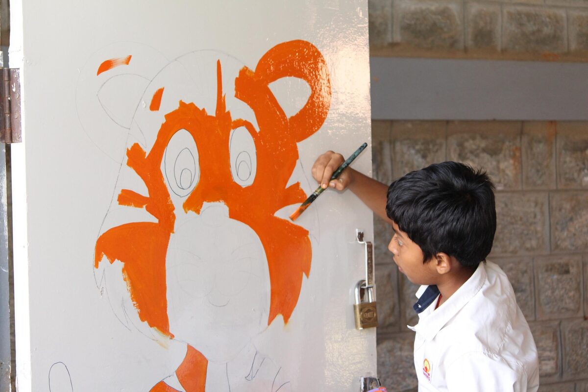 A student adding bold orange colour to a mural painting
