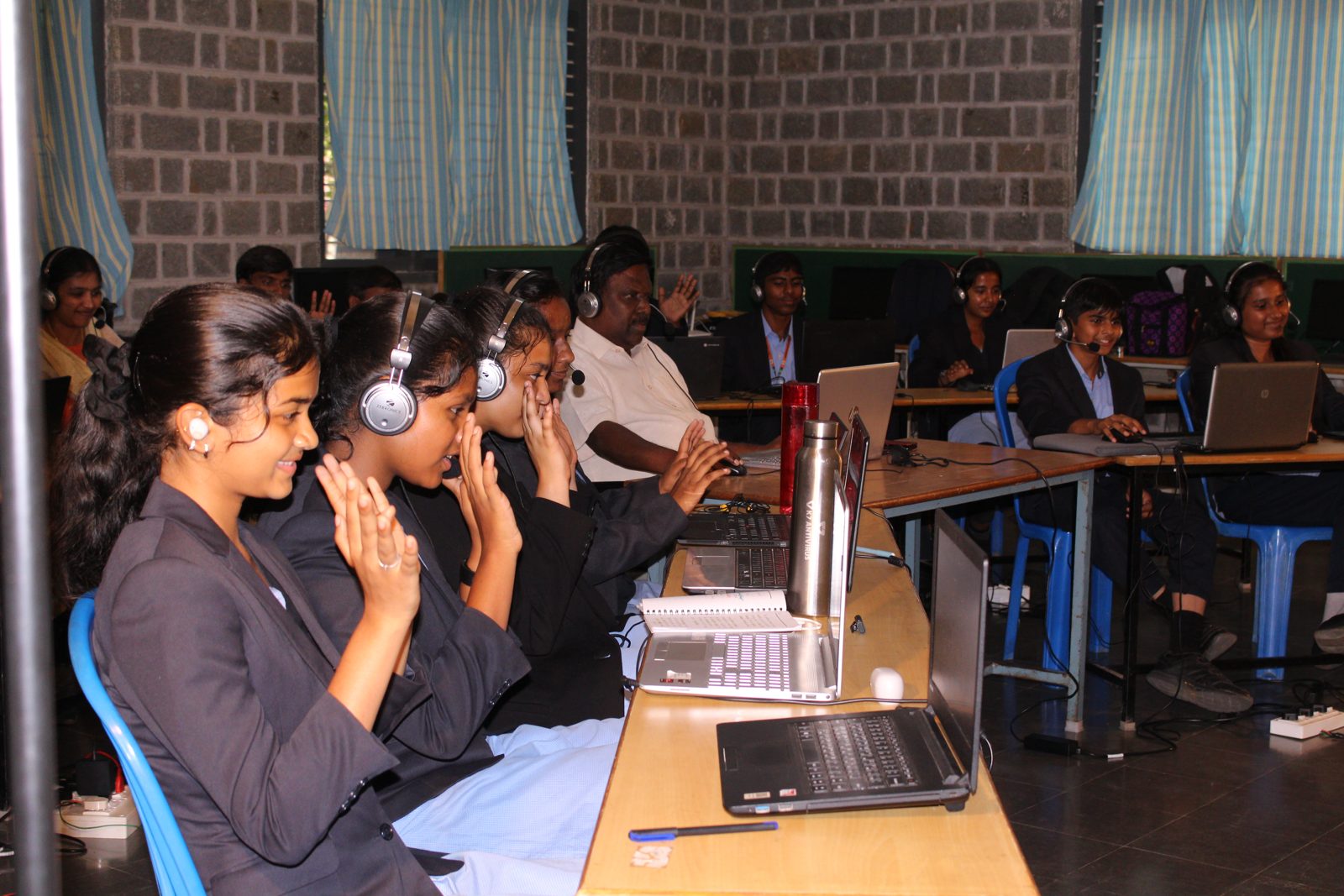 MMS students with headsets smiling and applauding during the live session with Korea in the Communication Lab
