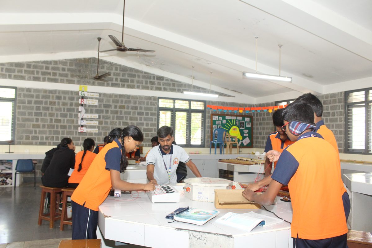 Students and a teacher gathered around the central workbench for a practical