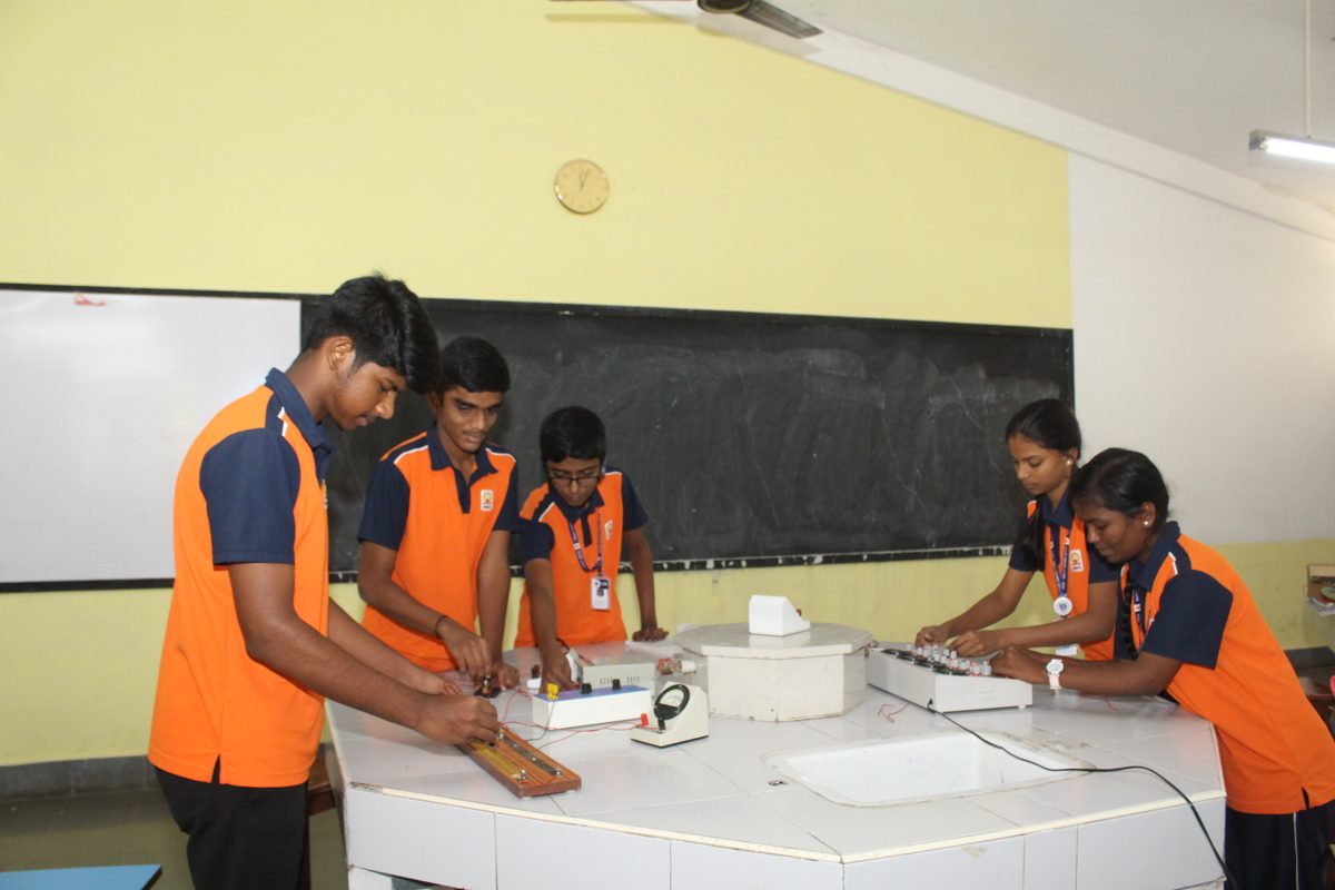 Students setting up a meter bridge on the physics lab bench in front of the blackboard