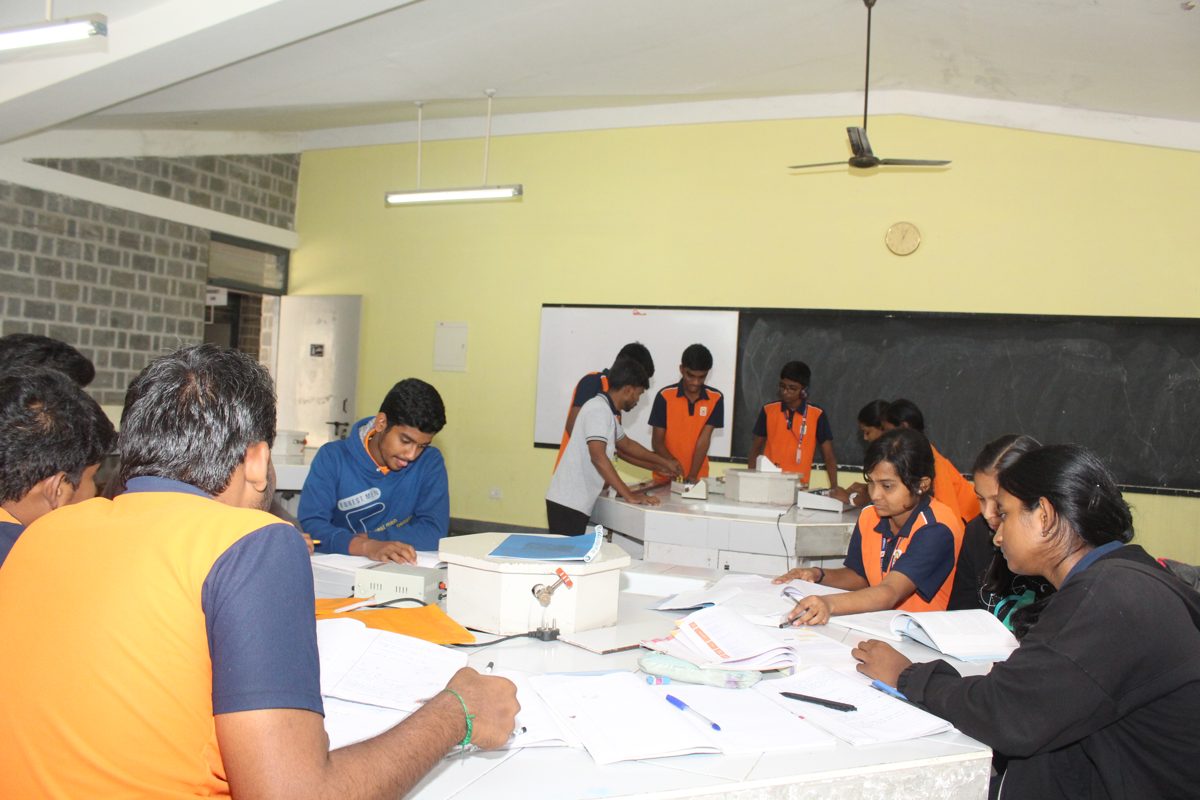 Students writing their readings in notebooks during a physics practical