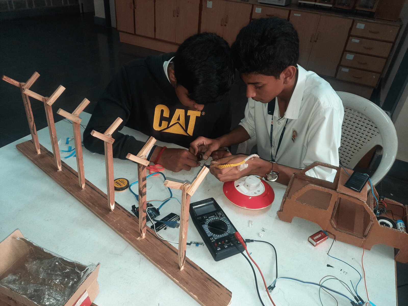 Two students testing the in-car receiver unit with a multimeter