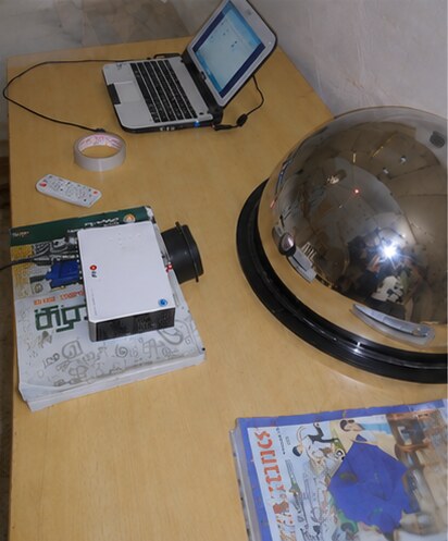 A laptop, projector, and convex spherical mirror set up on a workbench for the Version 1 planetarium's star-projection rig