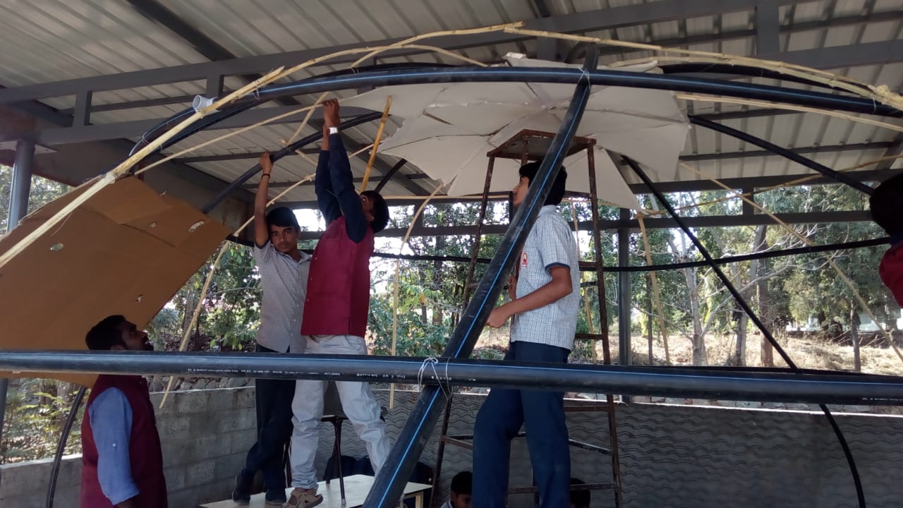Students and a teacher lifting a cardboard panel into place on the dome frame