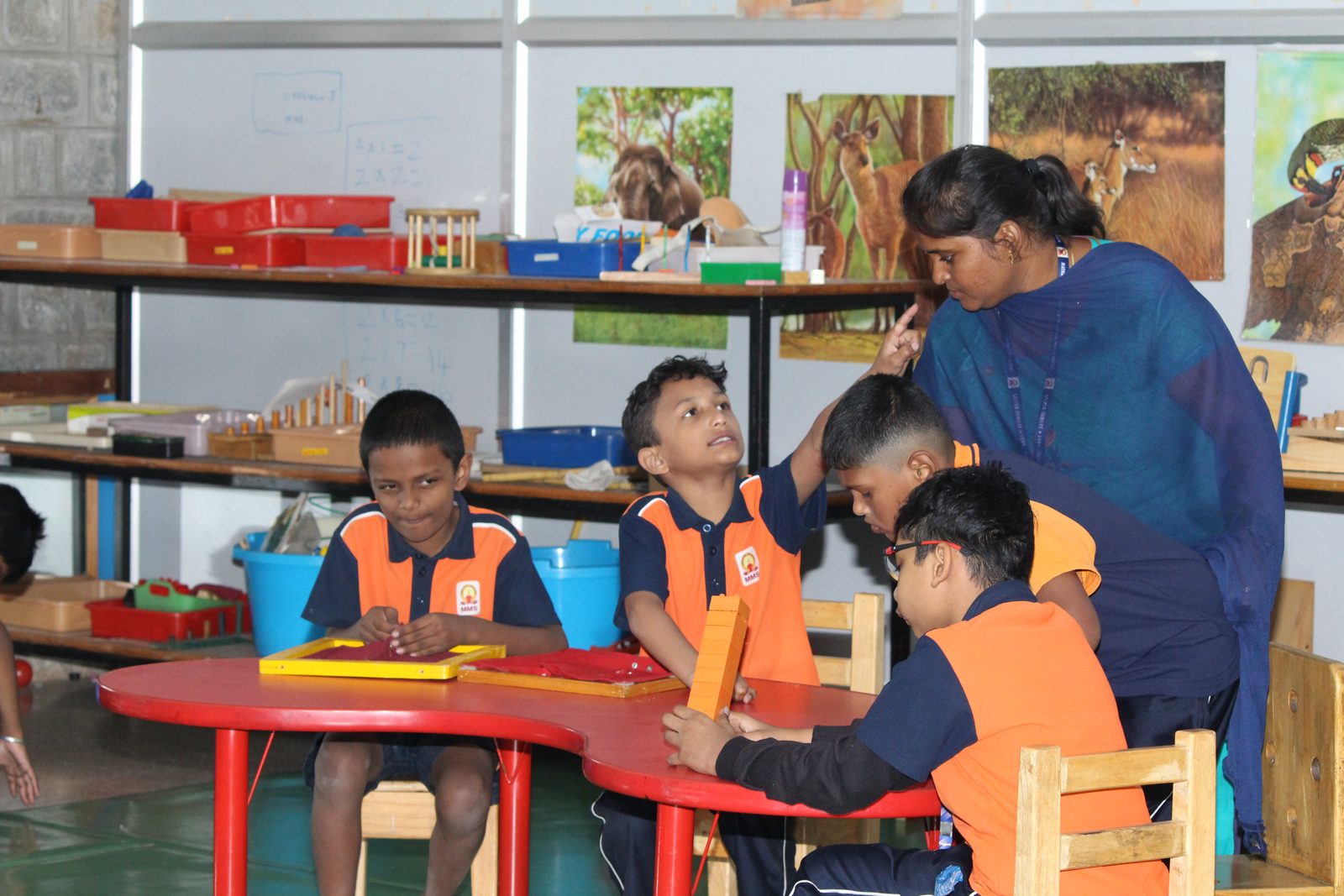 A special educator guiding students seated at a red table with learning materials