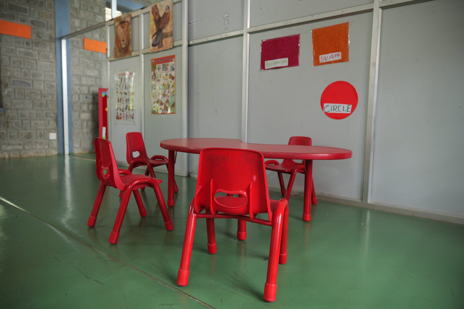 A bright classroom with a red table and chairs and learning charts on the walls