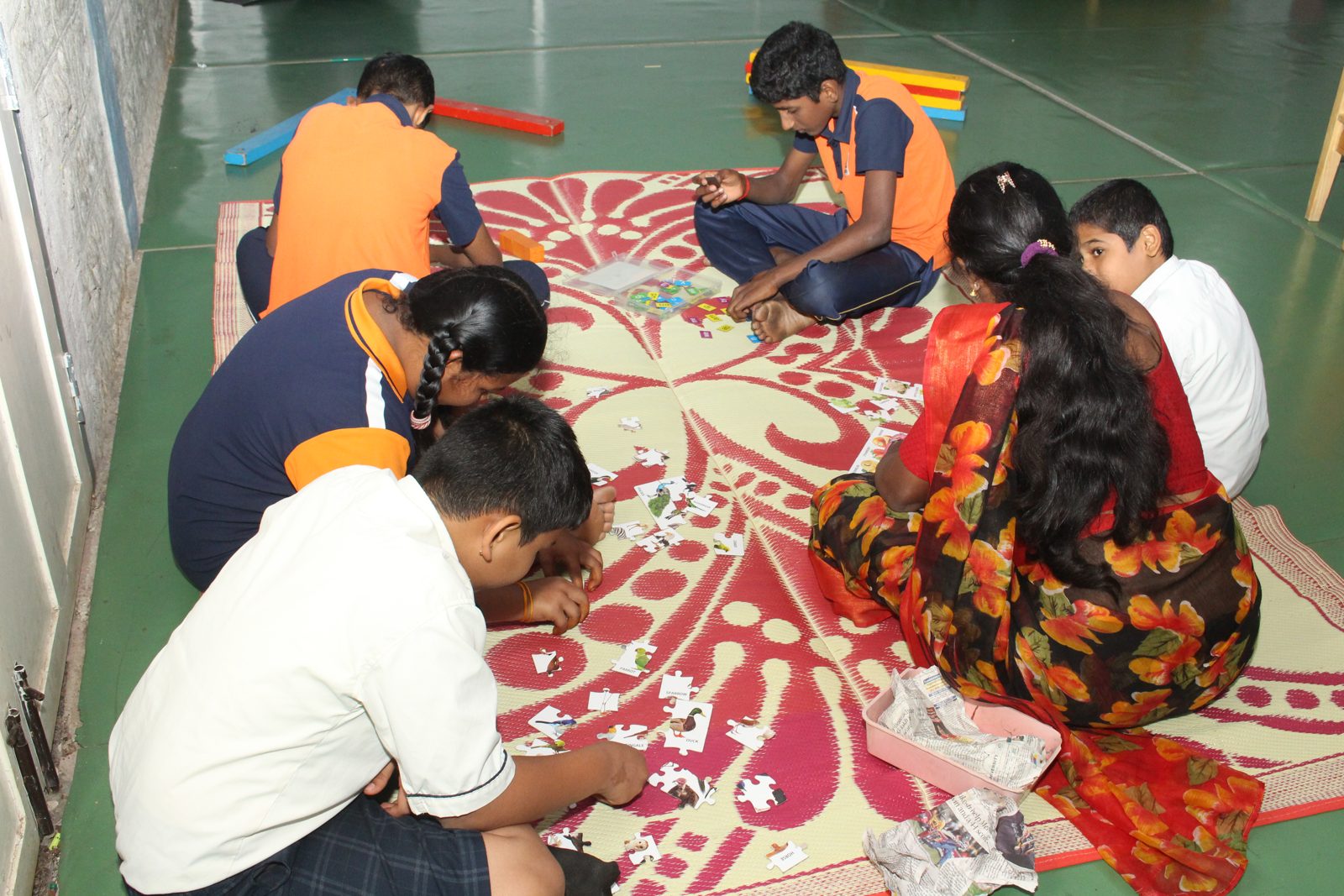 Students and an educator completing a jigsaw puzzle together on a floor mat