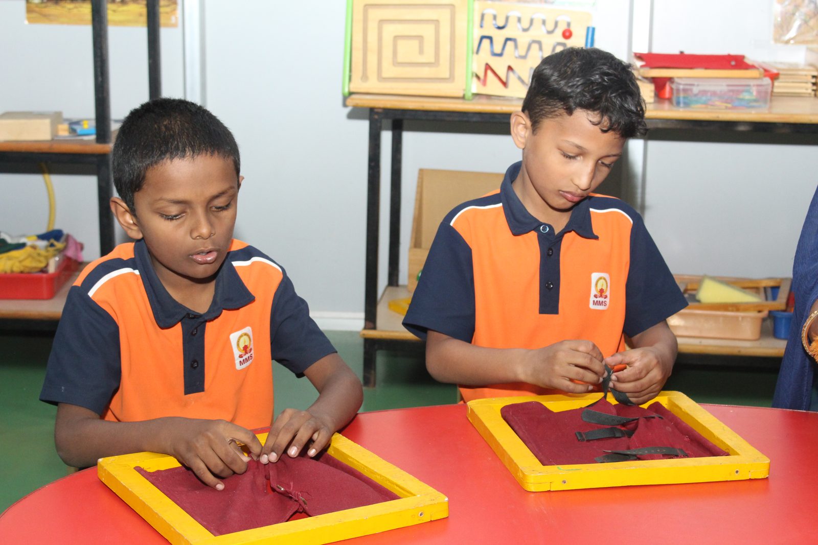 Two students working with tactile fabric frames at a red table