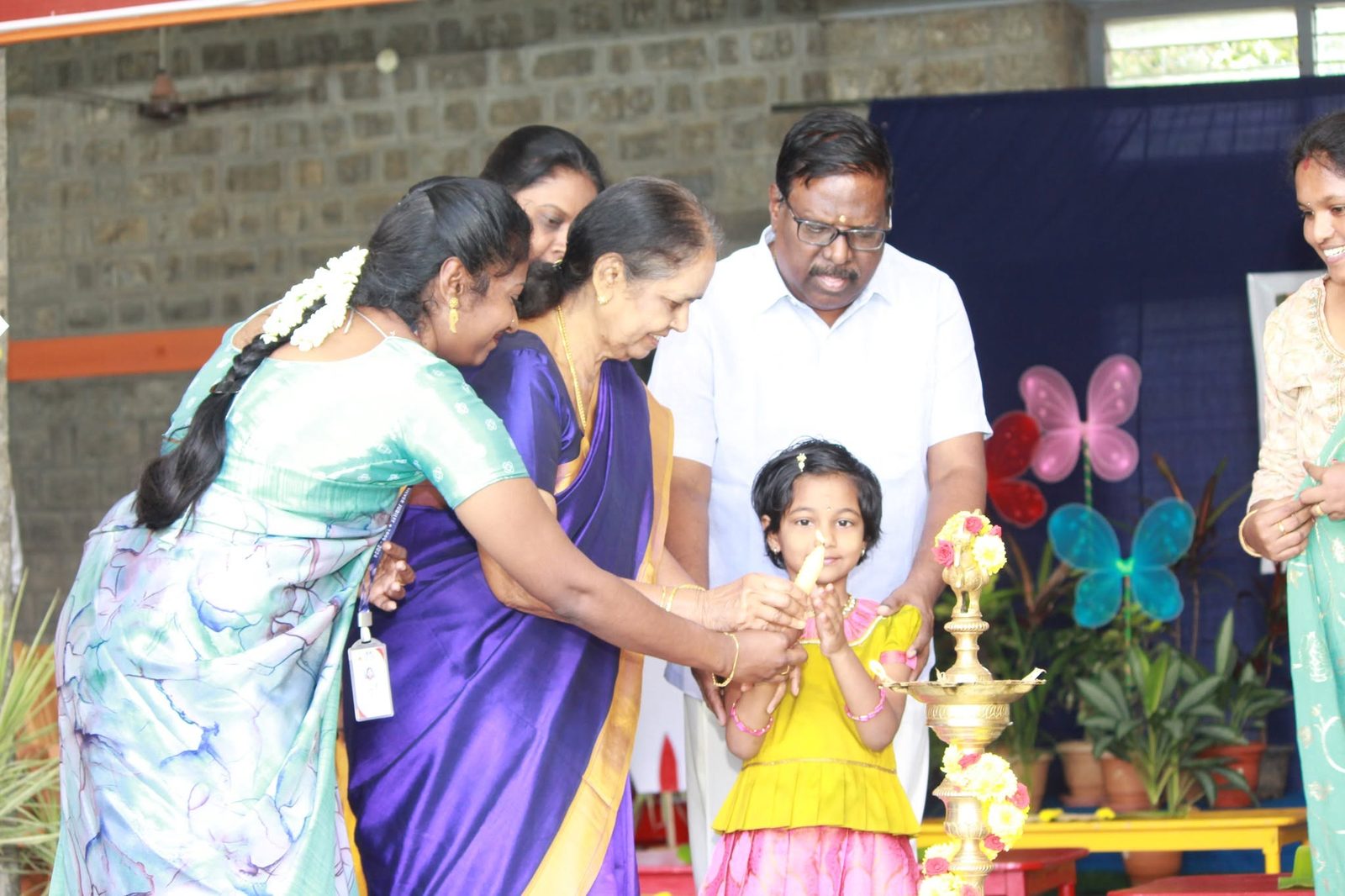A little girl lights the traditional lamp with the help of teachers and elders at the MMS Vidhyarambam
