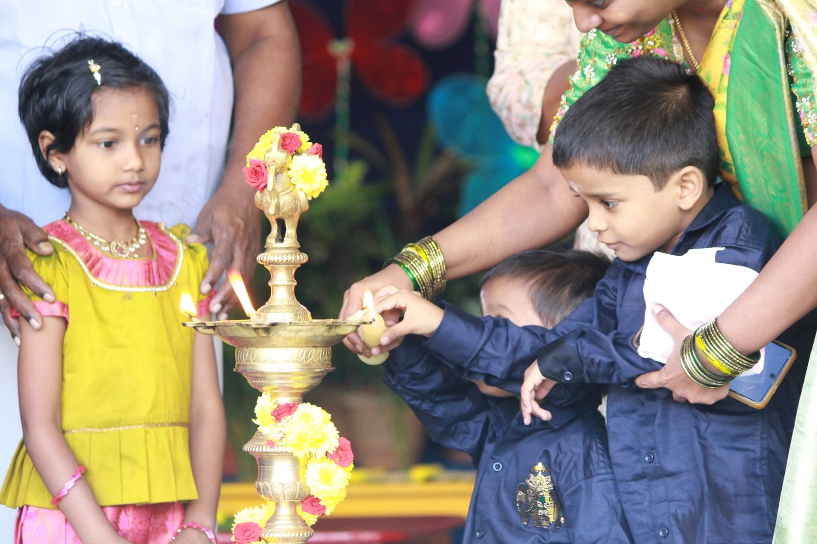 Young children and their mothers lighting the brass lamp decorated with flowers at MMS