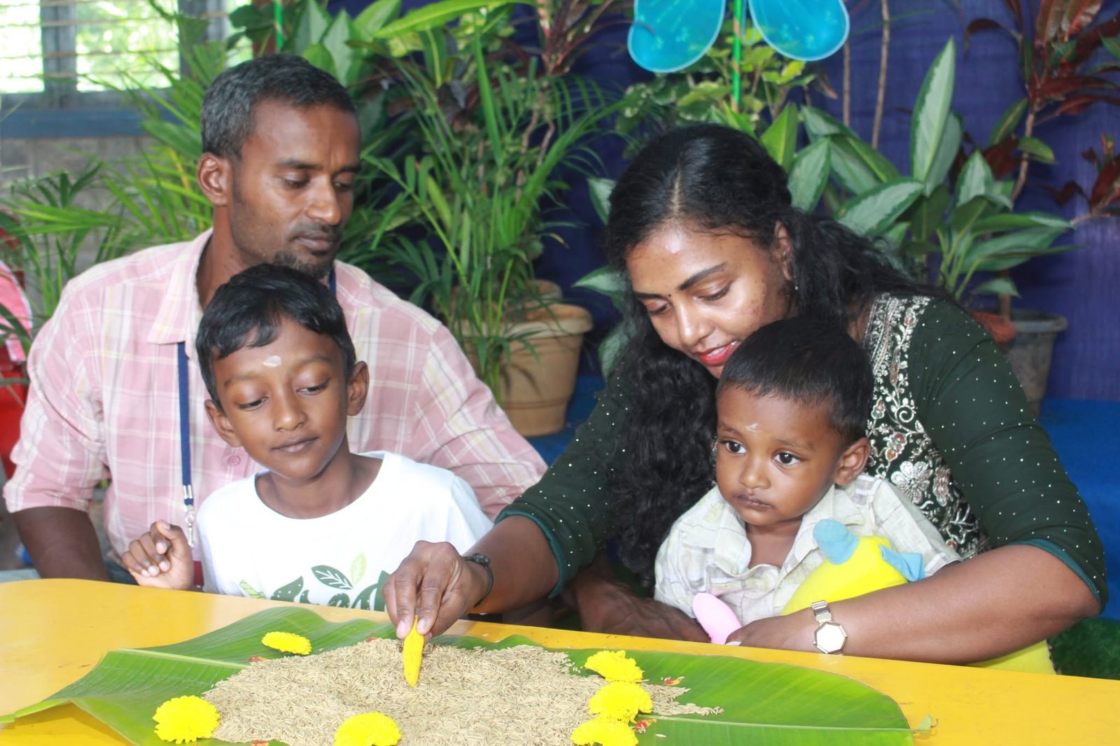 A father and mother help their young son write in the rice on a banana leaf