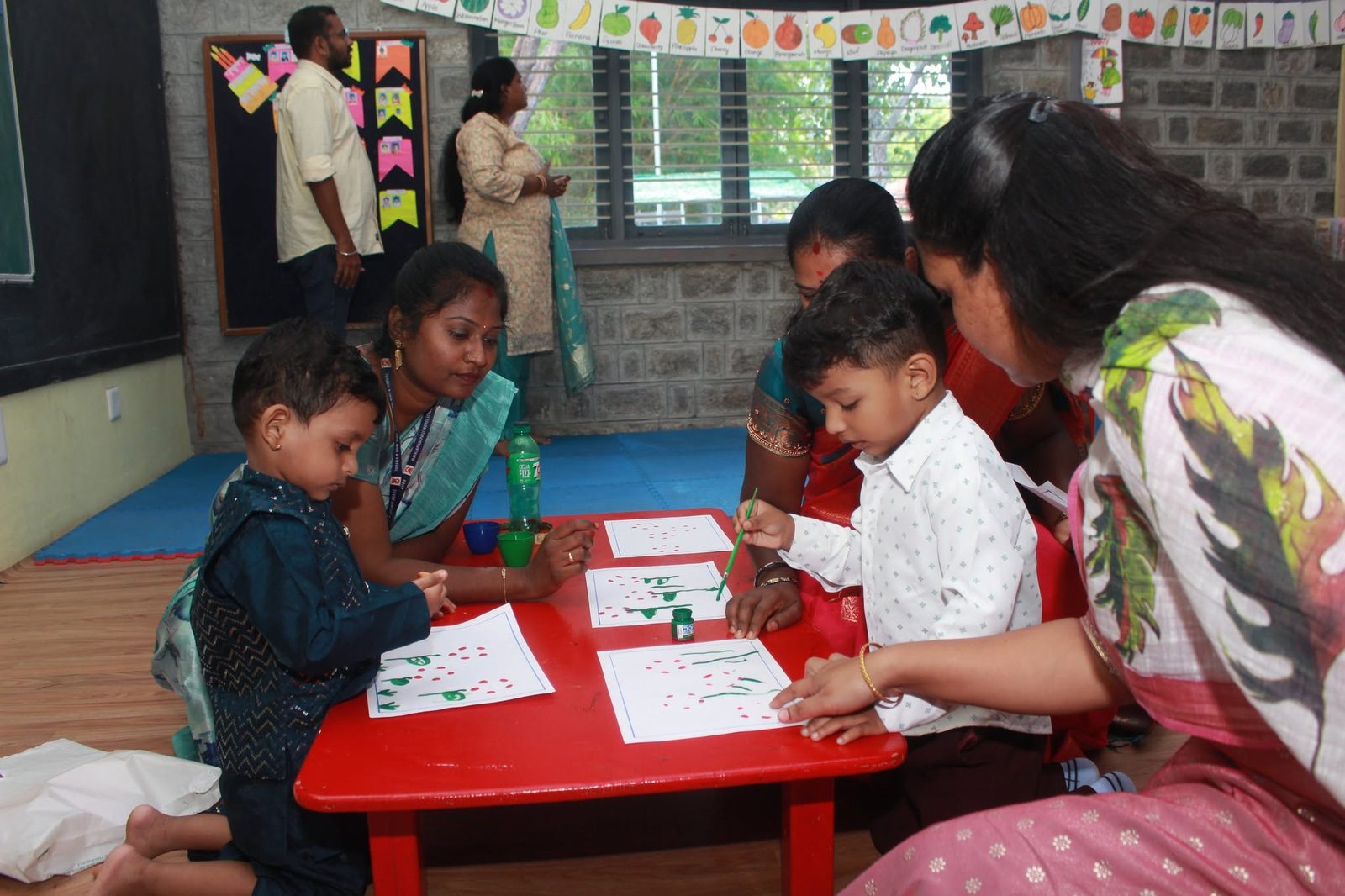 Children colour and draw at a table while teachers and parents sit beside them