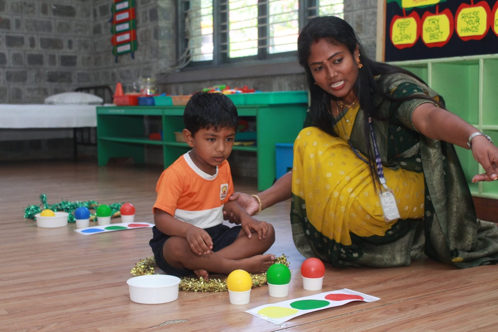 A teacher plays a colour-matching game with a small boy on the classroom floor
