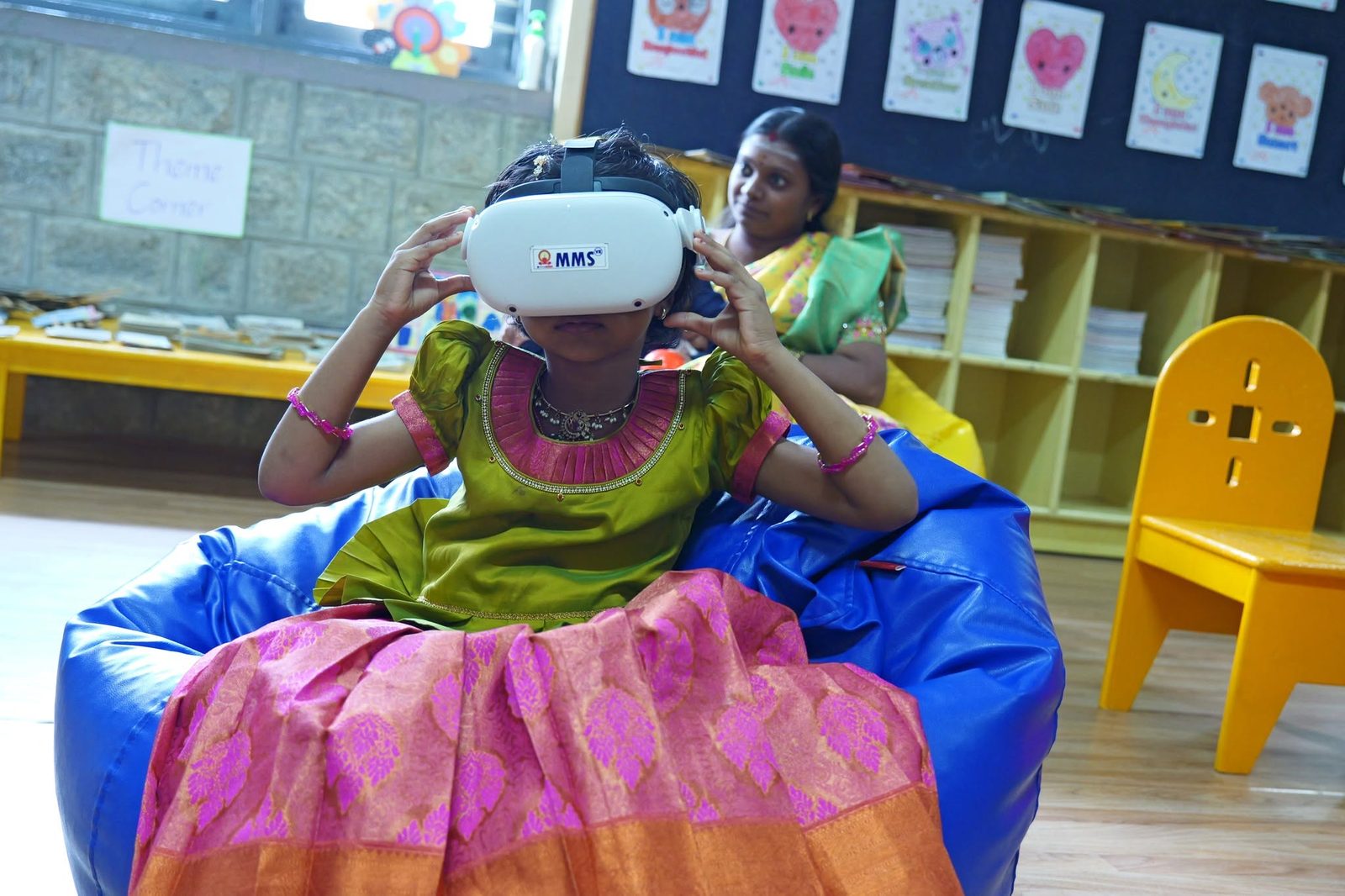 A girl in a traditional skirt explores a virtual reality headset while a teacher sits beside her